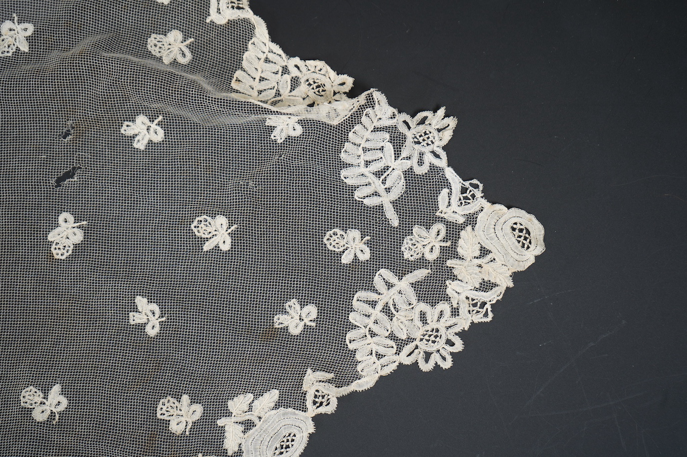 An Edwardian Brussels bobbin lace on net wedding veil, with all over bobbin lace appliqué spot motifs, within an ornate bobbin lace border, approximately 175cm x 168cm. Condition - there are various rust stains and holes